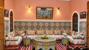 Una habitación tradicional marroquí con un sofá estampado, una mesa de centro decorativa y un tapiz grande en la pared.