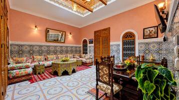 A traditional Moroccan interior with a patterned floor, a sofa set, a dining table with chairs, and a decorative mirror.