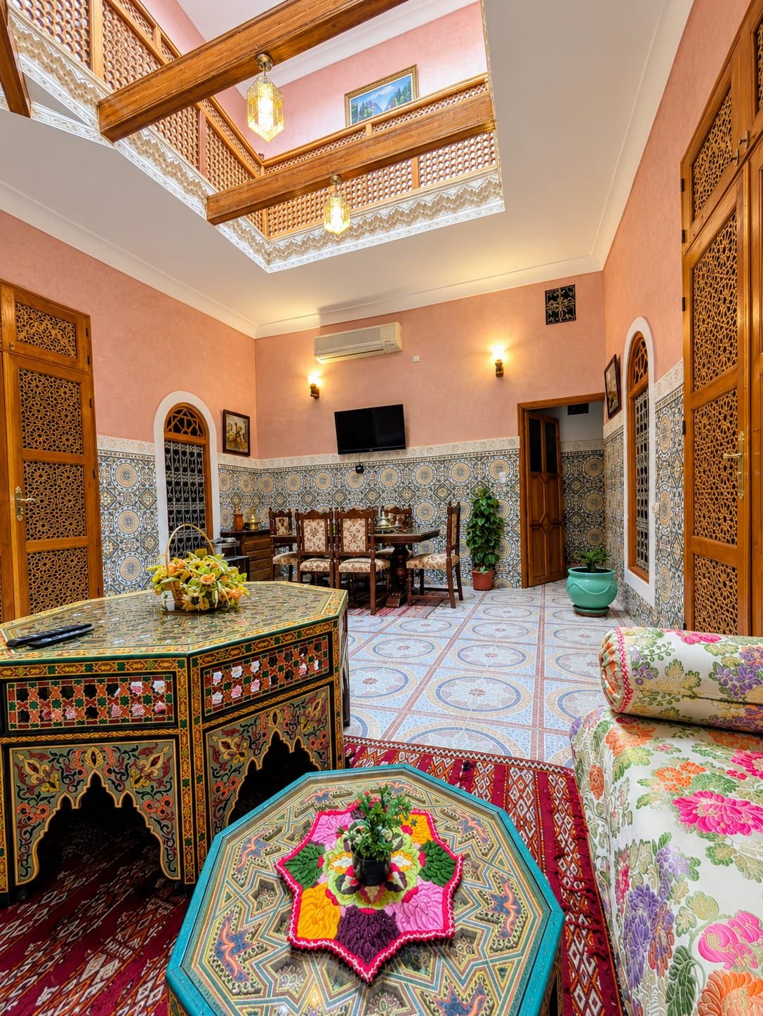 Una habitación con techo alto, televisor, zona de comedor con sillas y una alfombra decorativa.