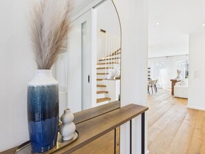 A modern interior with a wooden console table, a vase with dried plants, and a staircase leading to another room. - Boho Haus Sorpesee – Boutique Comfort & Private Wellness Right on Lake Sorpesee (Sundern (Sauerland))