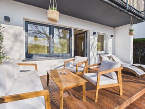 An outdoor seating area with wooden furniture and a table, large windows, and hanging planters. - Boho Haus Sorpesee – Boutique Comfort & Private Wellness Right on Lake Sorpesee (Sundern (Sauerland))