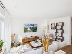 A modern living room with a large painting, a sofa, a coffee table, and a bookshelf. - Boho Haus Sorpesee – Boutique Comfort & Private Wellness Right on Lake Sorpesee (Sundern (Sauerland))