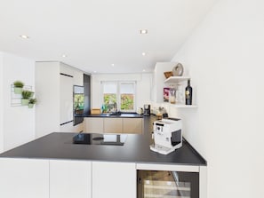 A modern kitchen with a black countertop, white cabinets, a coffee machine, and a window with a view of greenery. - Boho Haus Sorpesee – Boutique Comfort & Private Wellness Right on Lake Sorpesee (Sundern (Sauerland))