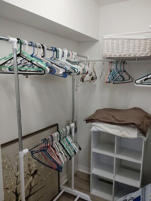 Un placard doté de plusieurs étagères et d’un espace pour suspendre les vêtements, organisé à l’aide de différents types de cintres, et sur lequel est plié un vêtement marron, placé à droite.