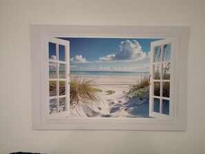 Ein gerahmtes Bild von einer Strandlandschaft mit blauem Himmel und Wolken.