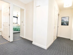 Ein Flur mit Teppichboden, weißen Wänden und einer Tür zu einem Schlafzimmer mit einem Bett.