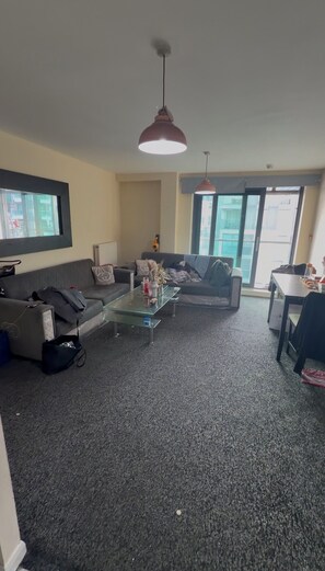 Ein Wohnzimmer mit Sofa, Couchtisch und Esstisch. Ein großes Fenster sorgt für natürliches Licht.