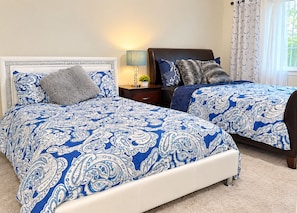 A bedroom with two beds, each with blue and white patterned bedding, a bedside table with a lamp, and a window with curtains. - Sassafras Oasis Sleeps 14 - All Season Retreat Near Barrie (Springwater)