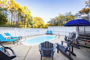 Un patio trasero con piscina, sillas de descanso y una terraza con sombrilla azul.