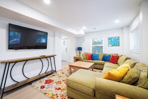 Una sala de estar con una televisión de pantalla plana montada en la pared, un conjunto de sofá, una mesa de centro y una alfombra estampada.