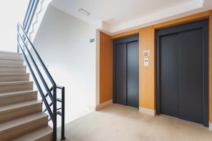 Un interior modern amb una escala, dos ascensors i un sòl de color clar.