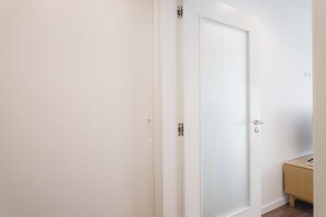 Una puerta blanca con un picaporte moderno y un pequeño armario de madera a la derecha.