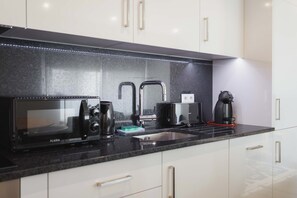 Una cocina moderna con encimera negra, electrodomésticos de acero inoxidable y armarios blancos.