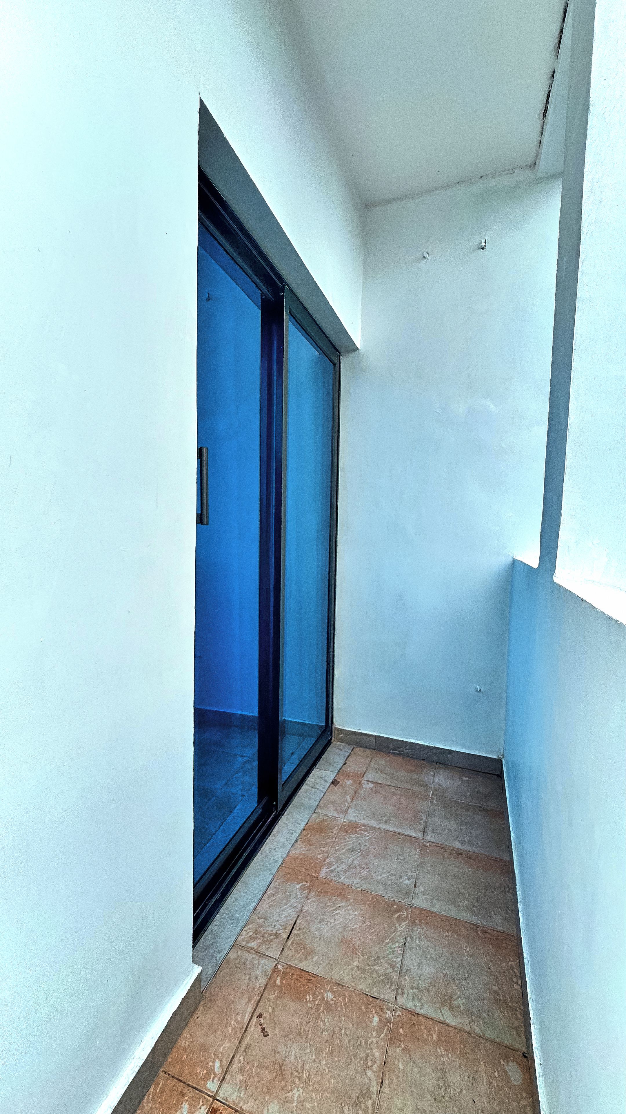 Een smalle gang met een blauwe glazen deur die leidt naar een balkon.