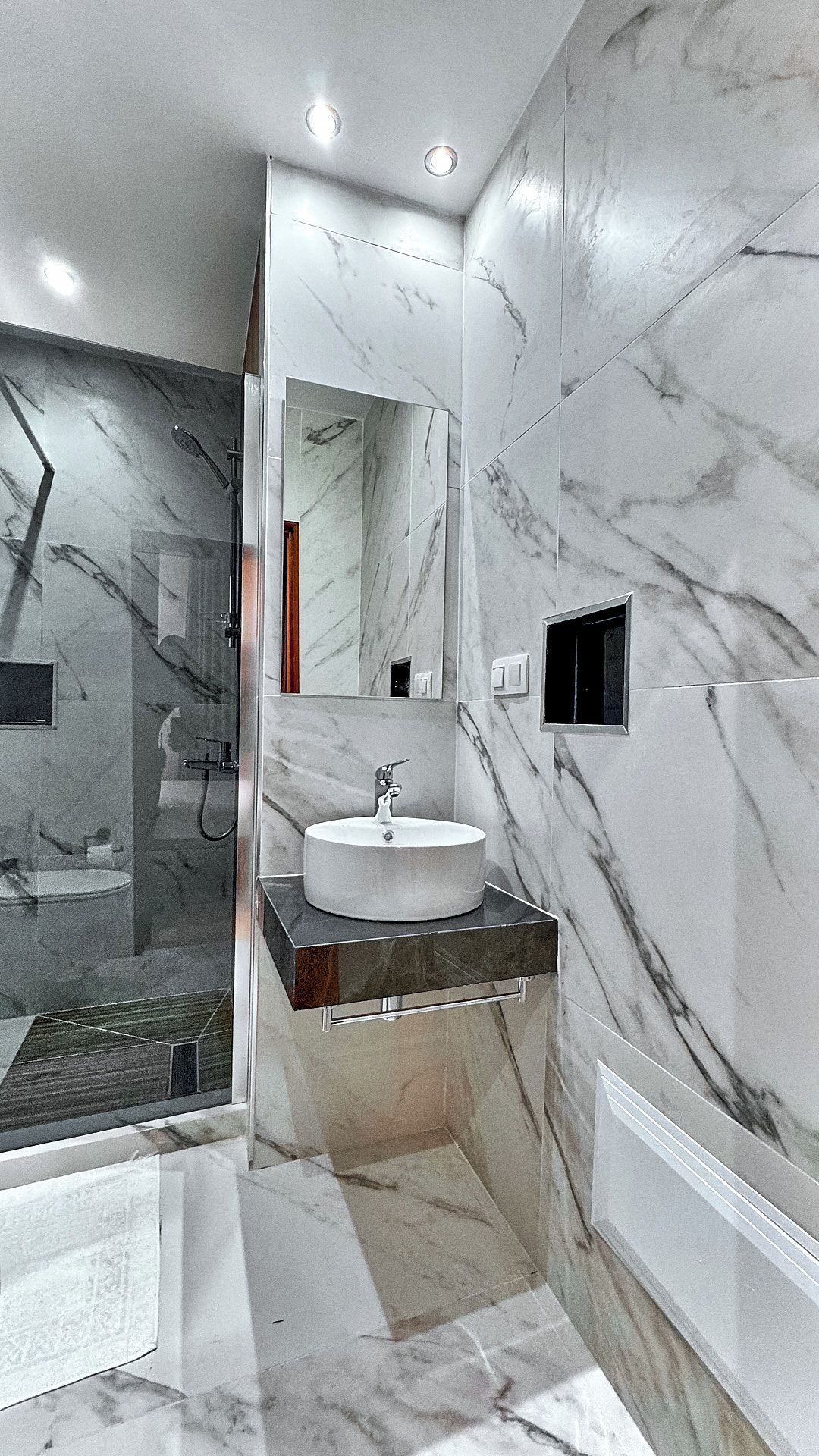 A modern bathroom with a marble sink, a glass shower enclosure, and a mirror.