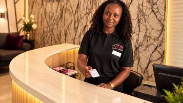 A hotel reception desk with a marble wall background, a framed portrait, and a modern, curved reception counter.