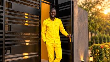 A person in a bright yellow uniform standing at a modern building entrance with a black gate.