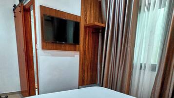 A hotel room with a bed, a television mounted on the wall, and a window with curtains.