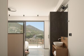 Ein modernes Badezimmer mit einem großen Spiegel, einem weißen Waschbecken und Bergblick durch eine Glastür.