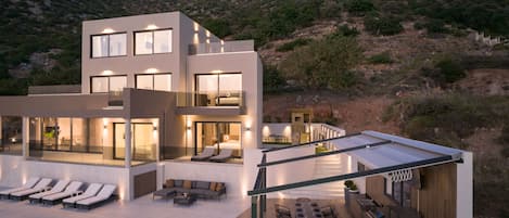 Un moderno edificio de varios pisos con piscina, asientos exteriores y vistas a un paisaje montañoso.