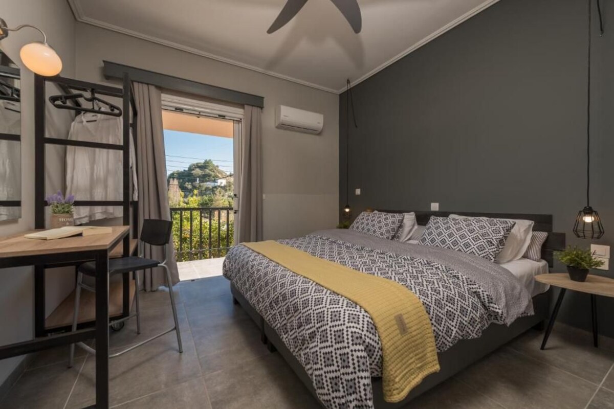 A bedroom with a bed, a desk, a chair, a small table, and a balcony with curtains.