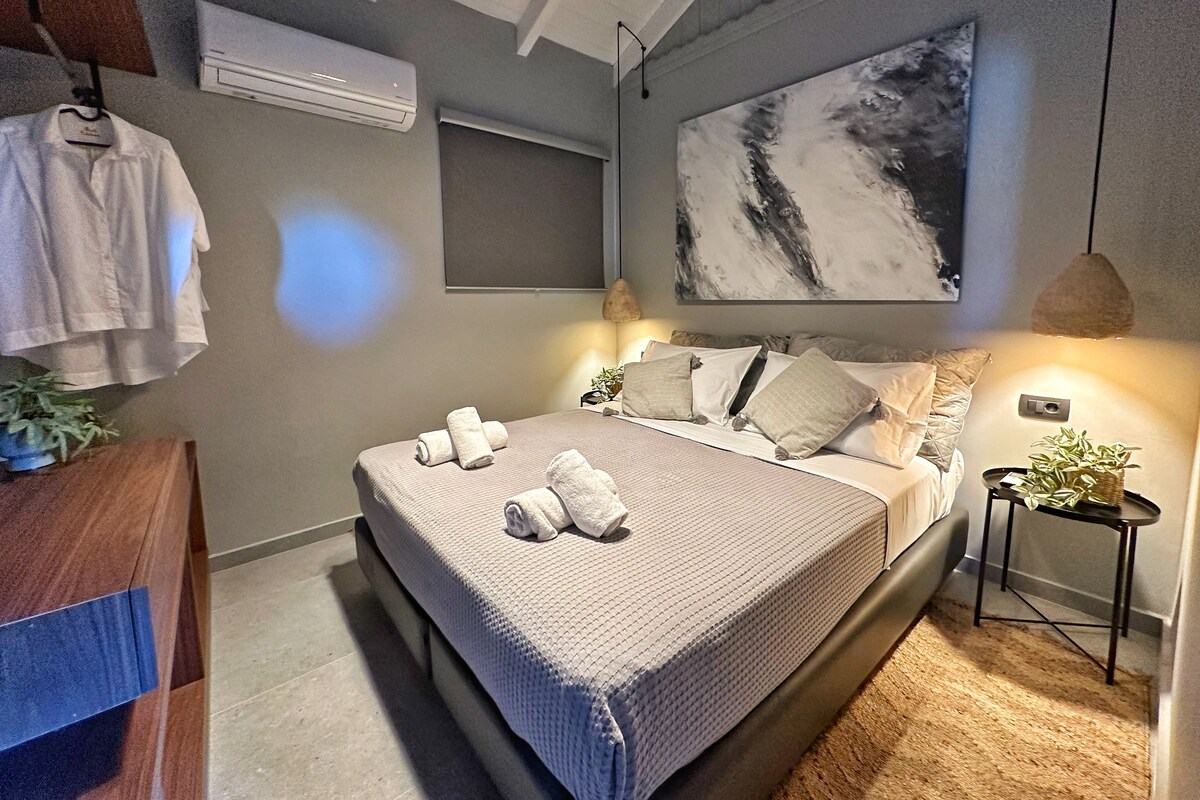 A modern bedroom with a large bed, a wall-mounted air conditioner, and a painting.