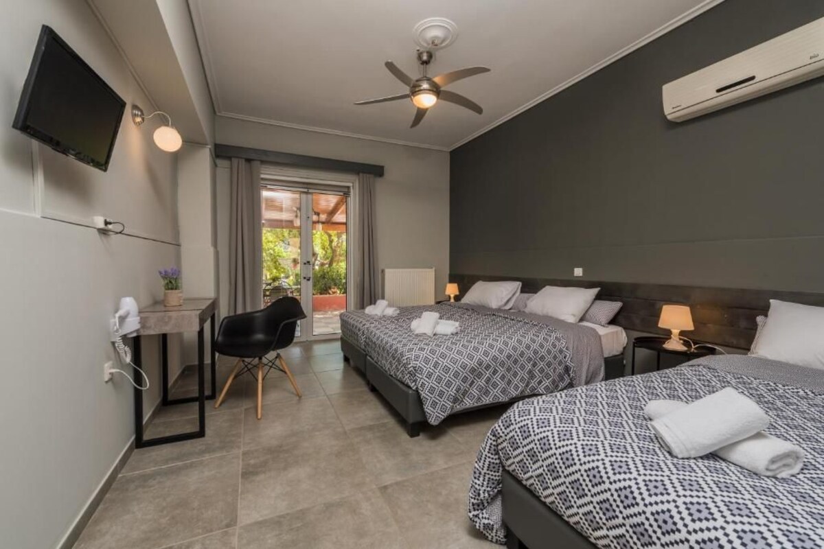 A hotel room with two beds, a desk, a chair, a TV, and a ceiling fan.