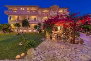 A multi-story hotel with a stone-paved courtyard, outdoor seating, and a well-lit entrance. - Filoxenia Luxury Studios & Apartments (Zakynthos)