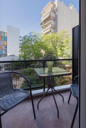 A balcony with two wicker chairs and a glass table, overlooking a cityscape with buildings and trees. - Minimal City View Apartment (Kallithea)