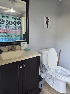 Een badkamer met een wit toilet, een wastafel met een spiegel erboven en een bordje aan de muur.