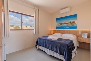 Una habitación de hotel con cama, un cuadro, una ventana con cortinas y un equipo de aire acondicionado.