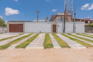 A paved area with a stone pathway leading to a building with two garage doors. - Casa Guerreiro - Elegance in Cumbuco by Carpediem (Caucaia)