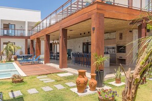 A covered outdoor area with a pool, lounge chairs, and a barbecue grill. - Casa Guerreiro - Elegance in Cumbuco by Carpediem (Caucaia)