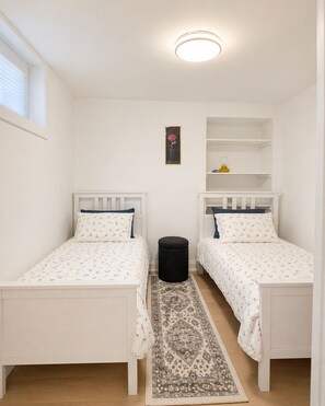 A bedroom with two single beds, a small rug, a nightstand, a shelf with a lamp, and a framed picture on the wall. - Self-Contained, Full Kitchen, Full Bath, Private-A (Richmond Hill)