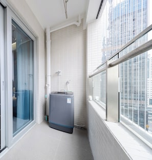 A modern bathroom with a glass shower enclosure, a grey washing machine, and a view of a cityscape through large windows. - Gepai Cityview Hotel Futian Expo (Shenzhen)