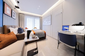 A modern hotel room with a bed, a desk, a chair, a sofa, and a television.