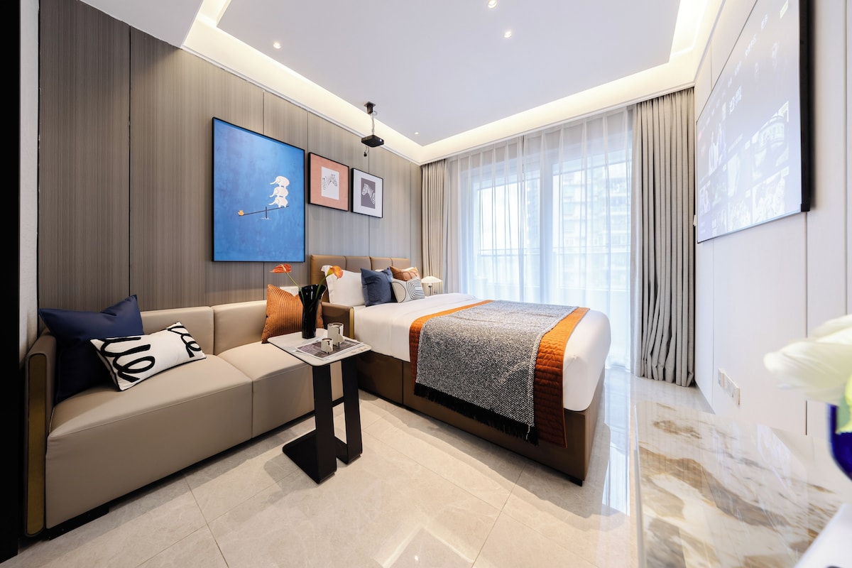 A modern hotel room with a bed, a sofa, a coffee table, and a TV screen.