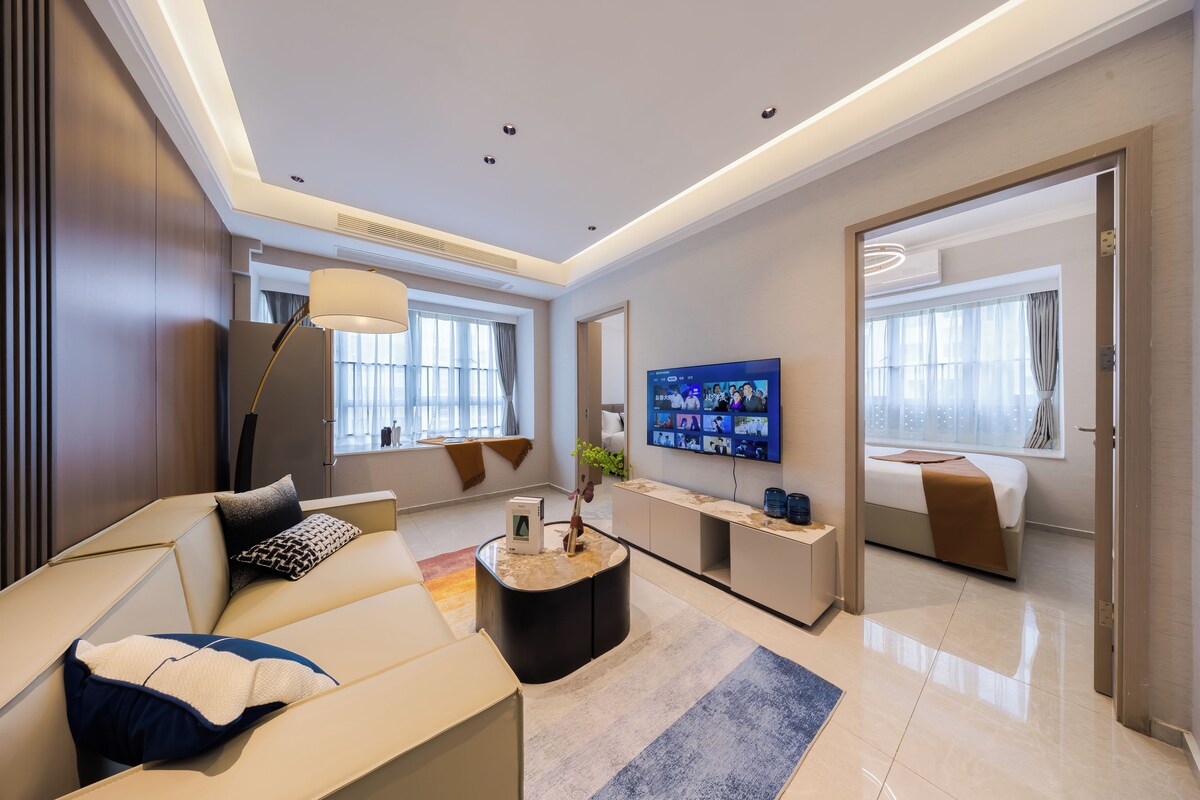 A modern hotel room with a sofa, a coffee table, a TV, and a bed.