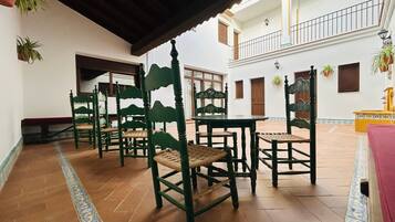 A courtyard with tiled flooring, green wooden chairs, a bench, and a yellow table.