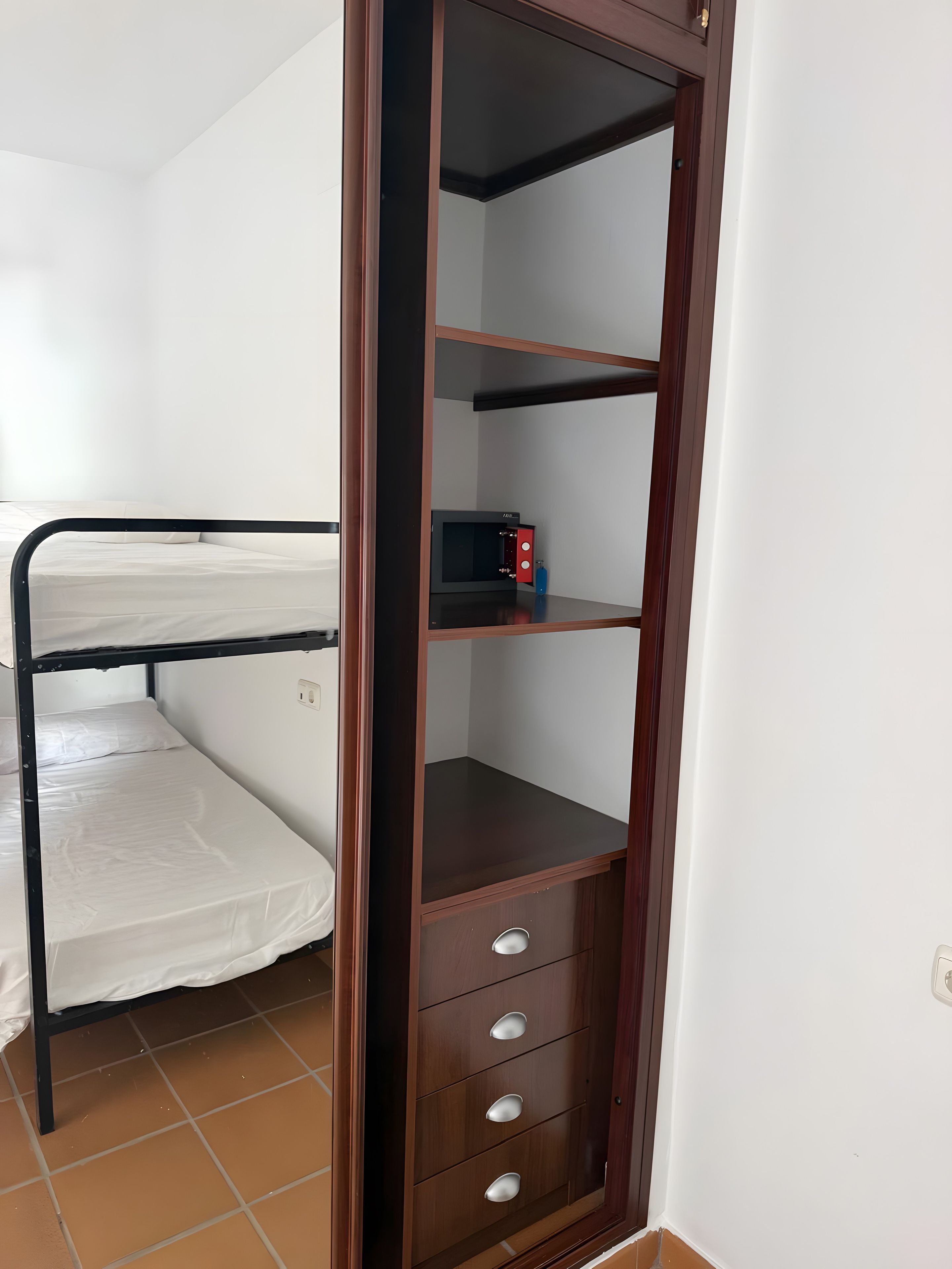 A room with a bunk bed, a wooden wardrobe with drawers, and a microwave on the shelf.