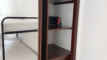 A room with a bunk bed, a wooden wardrobe with drawers, and a microwave on the shelf.