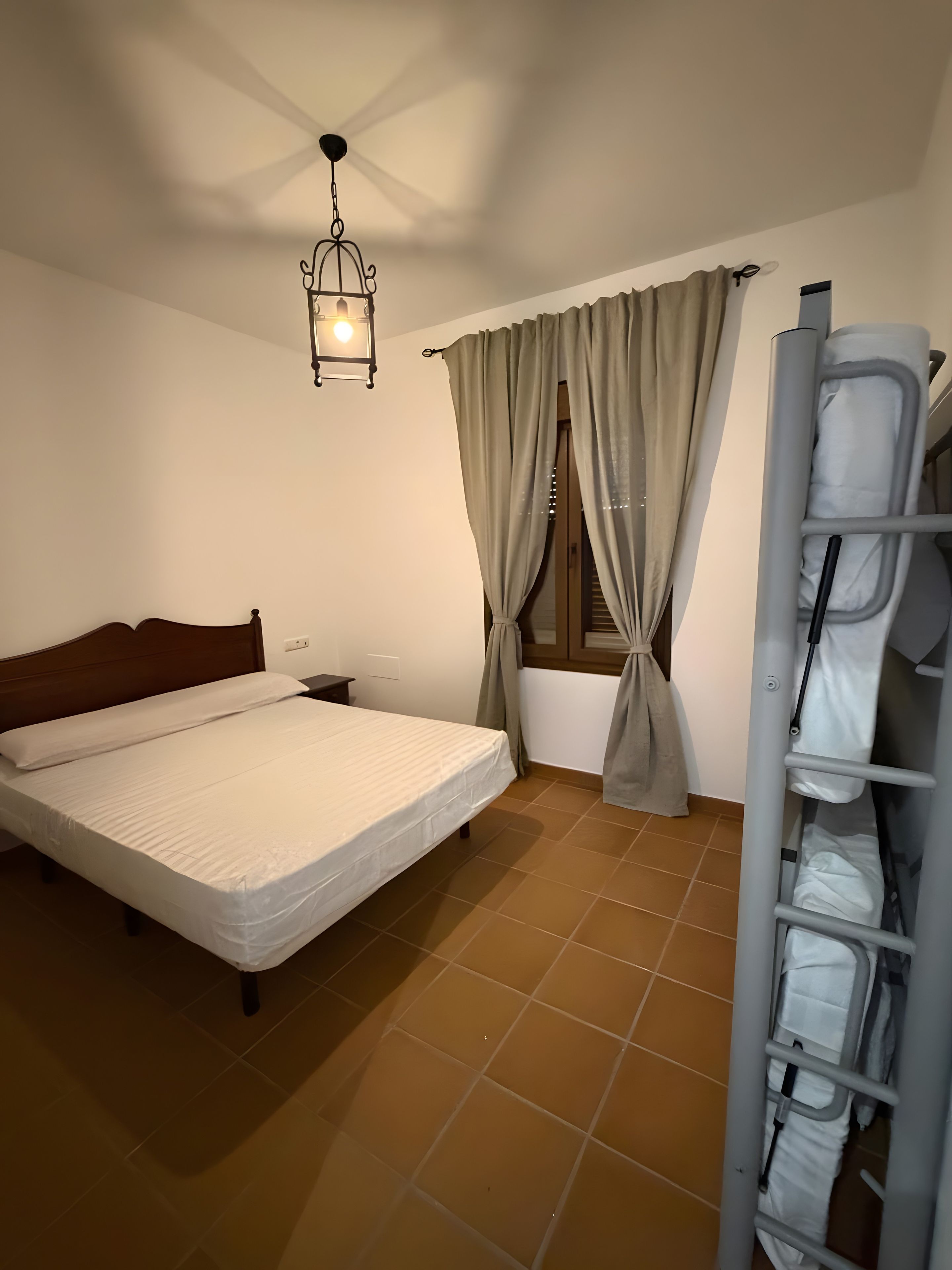 Une chambre à coucher comprenant un lit, une table de chevet, un luminaire suspendu, une fenêtre avec des rideaux et une armoire intégrée.