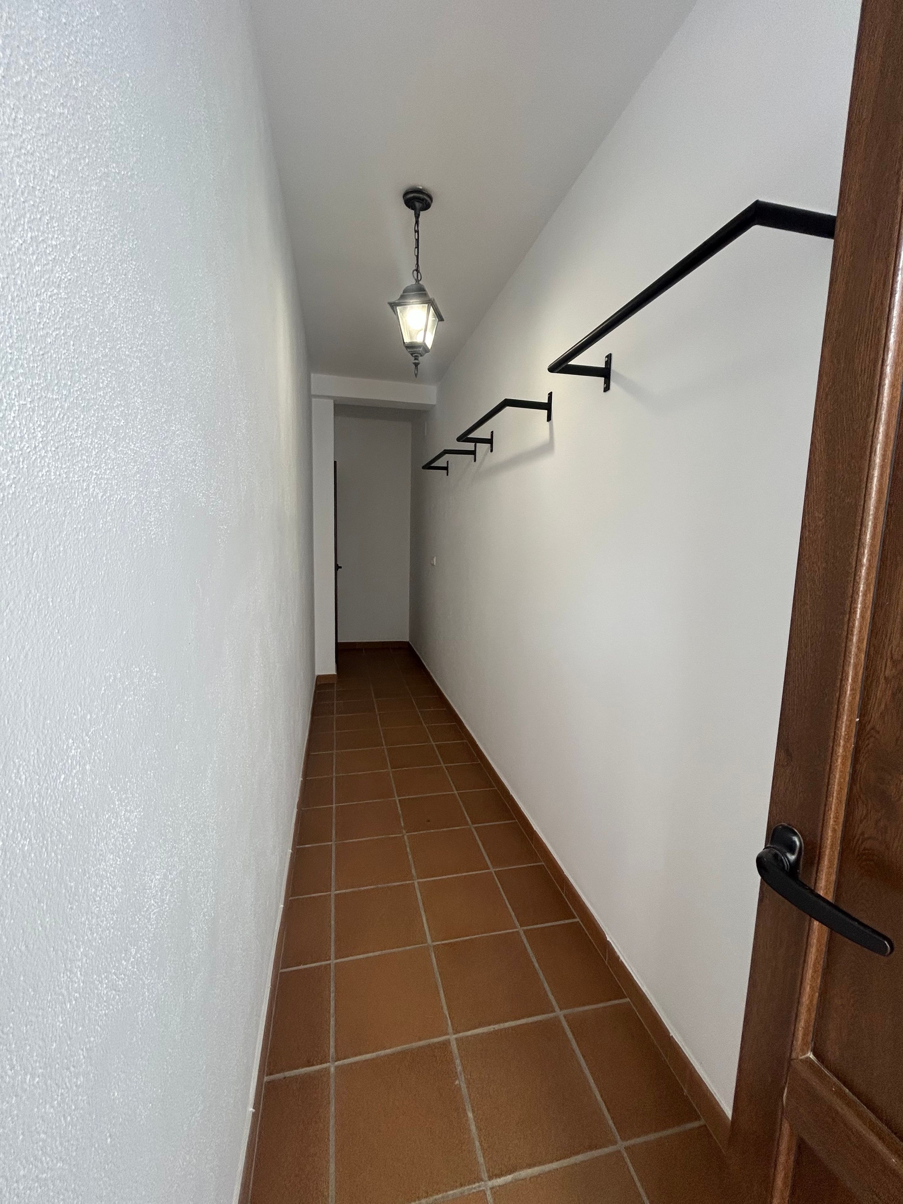 Un couloir doté d’un sol carrelé, d’un luminaire au plafond et d’une porte avec une poignée noire.