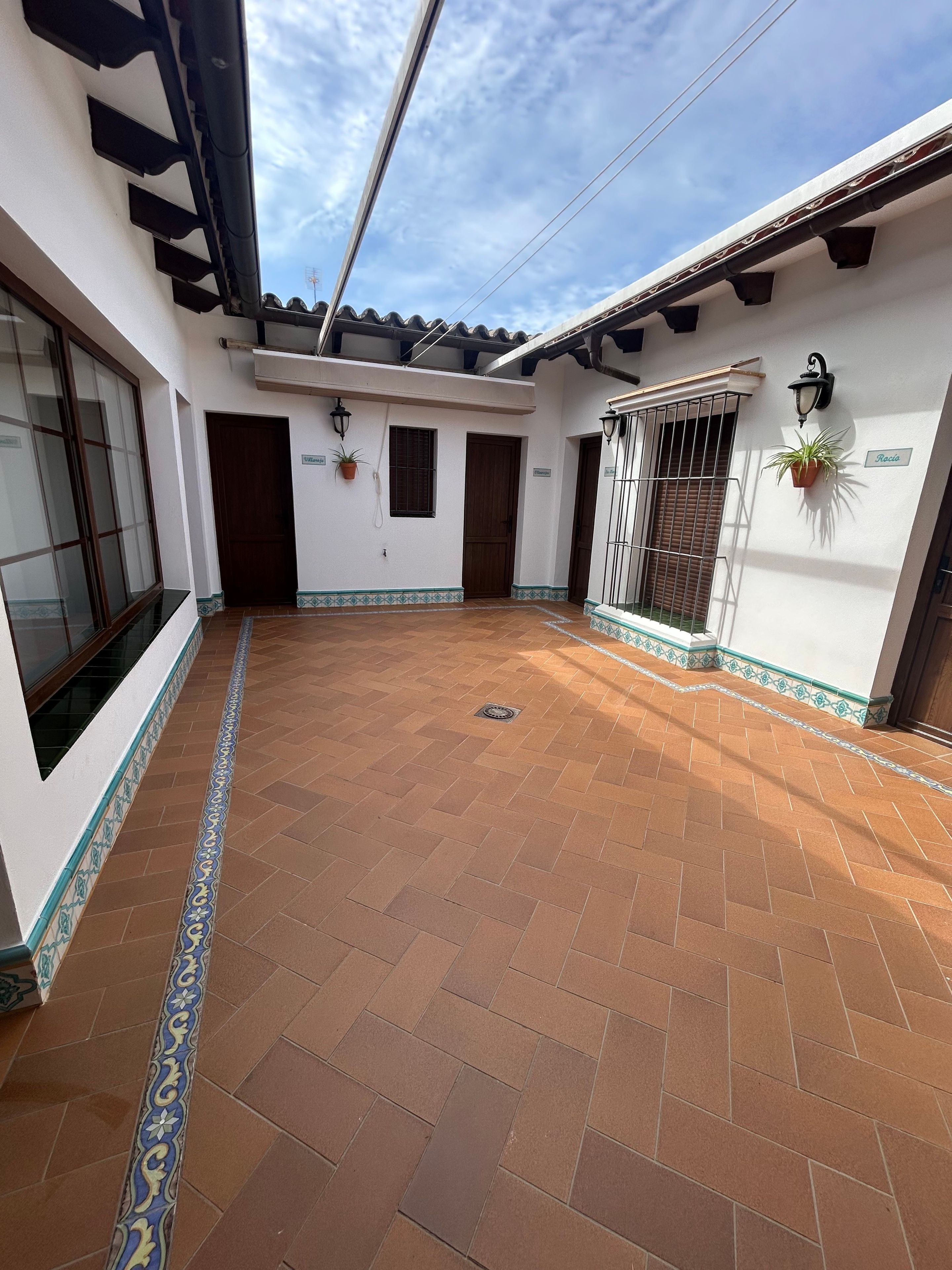 Un patio con suelo de baldosas, una puerta de madera y una ventana con reja de metal.