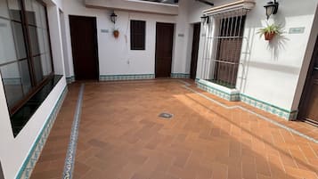 Un patio con suelo de baldosas, una puerta de madera y una ventana con reja de metal.
