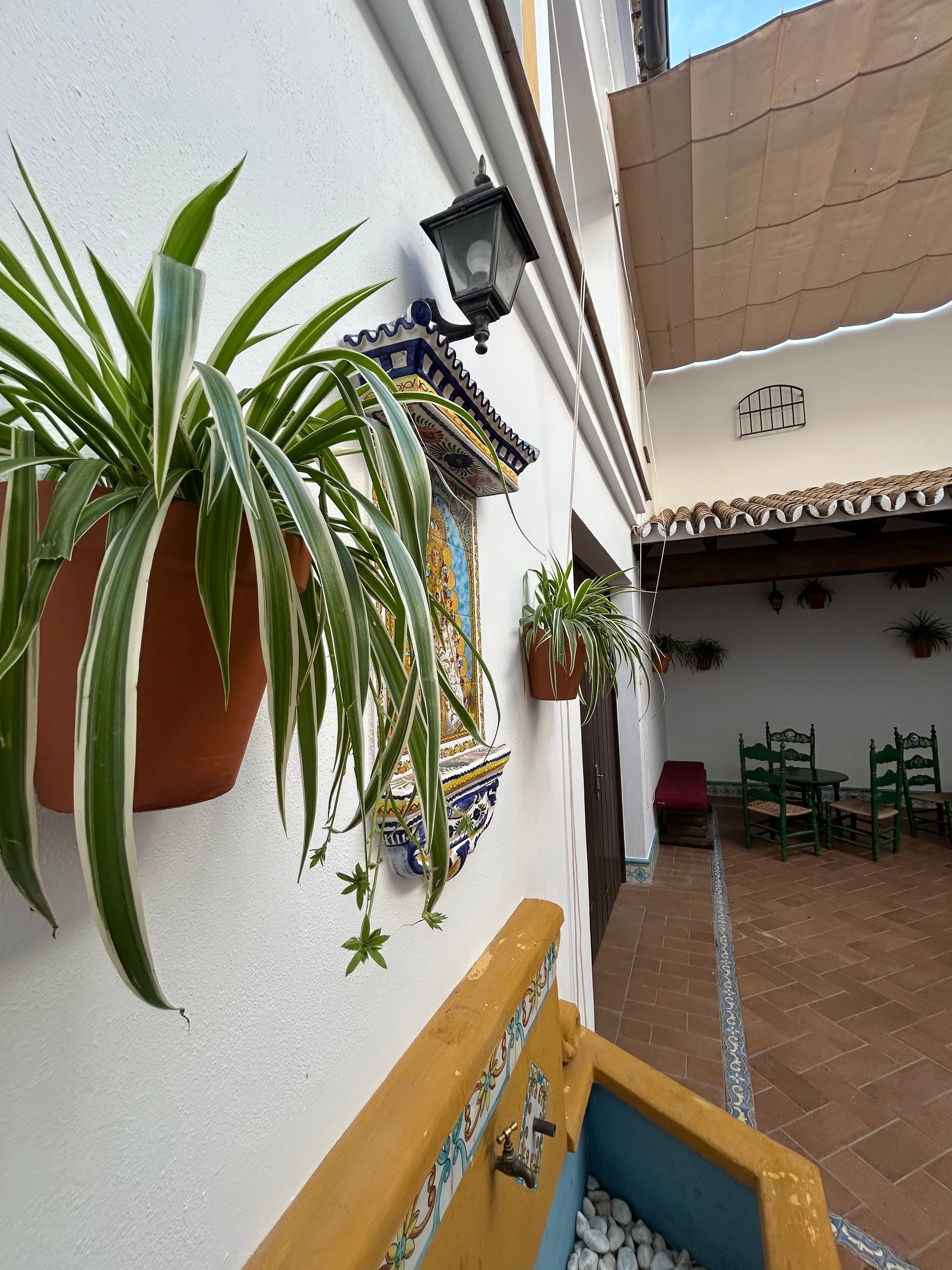 A courtyard with potted plants, a wall-mounted light fixture, a tiled floor, and a small seating area with chairs.