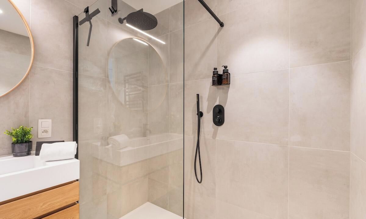 Et moderne badeværelse med en glasbrusekabine, en hvid vask og en lille hylde med toiletartikler.