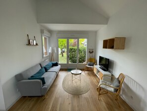 A living room with a sofa, chairs, a TV, and a view through a glass door. - Holiday Home 'Family Home à 400 m de la plage Mauret' with Garden and Wi-Fi (Andernos-les-Bains)
