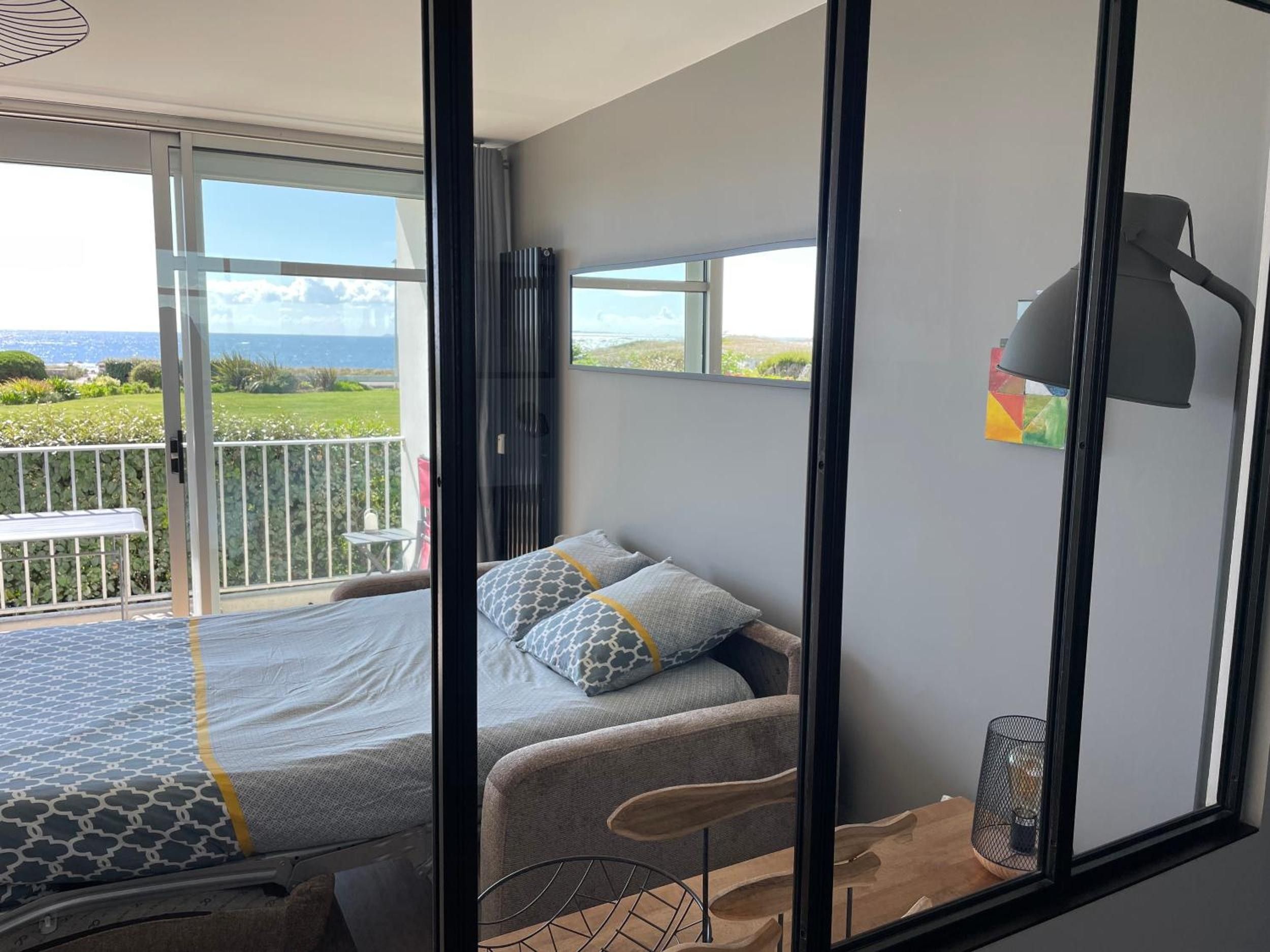 A bedroom with a bed, a chair, a lamp, and a view of the outdoors.