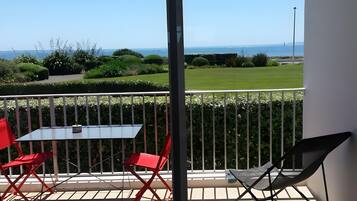 A balcony with a table and chairs, a view of the sea, and a well-maintained garden.